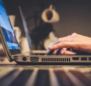 Donkere afbeelding van een laptop, waarop een persoon aan het typen is. 