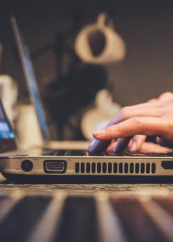 Donkere afbeelding van een laptop, waarop een persoon aan het typen is. 