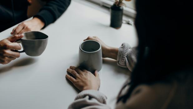 Twee mensen aan tafel met kopjes in hun hand
