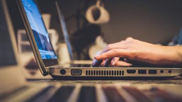 Donkere afbeelding van een laptop waarop een persoon aan het typen is.